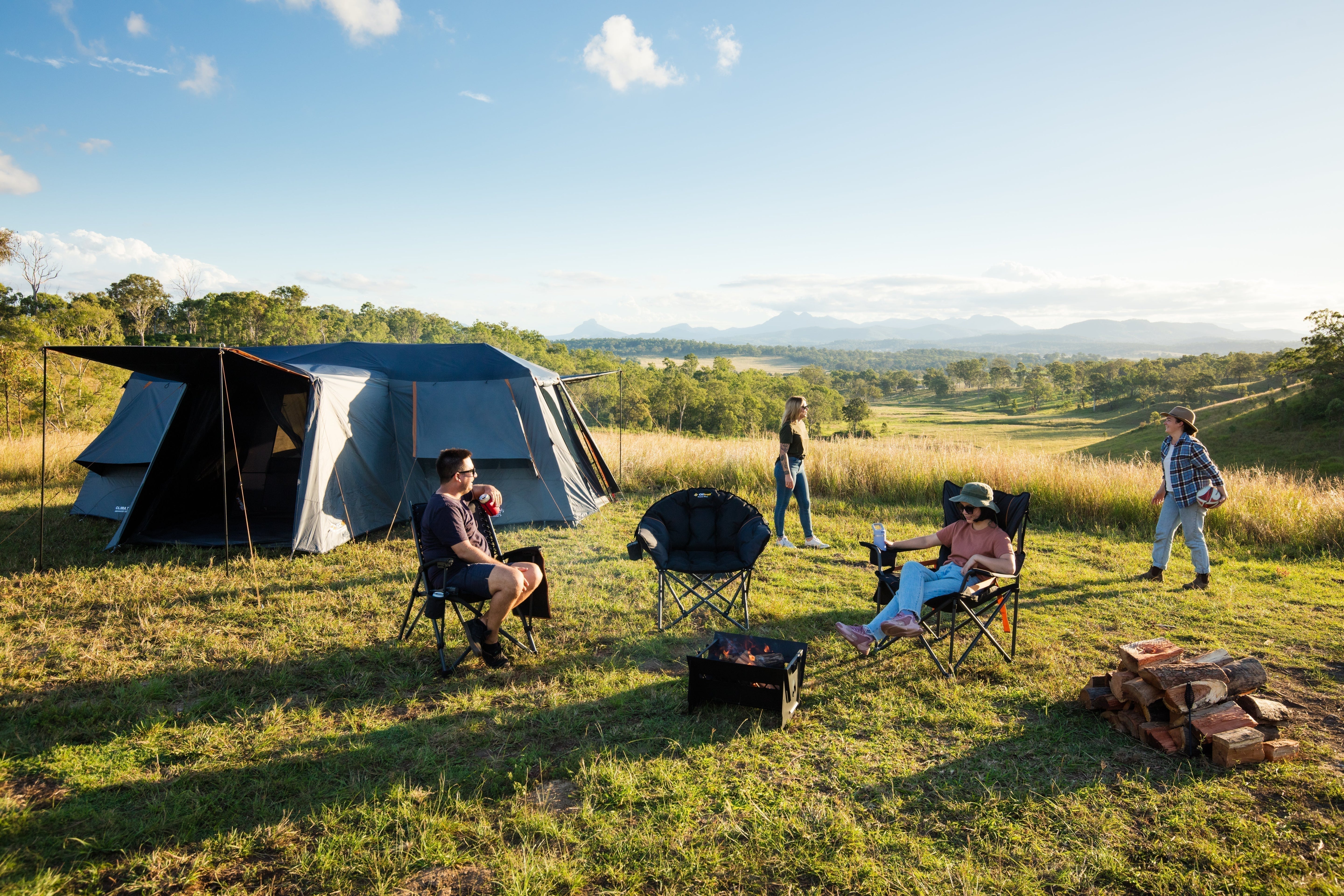 Fast Frame BlockOut Lumos 12P Tent set up on a grassy hill as people relax around a campfire with mountain views.