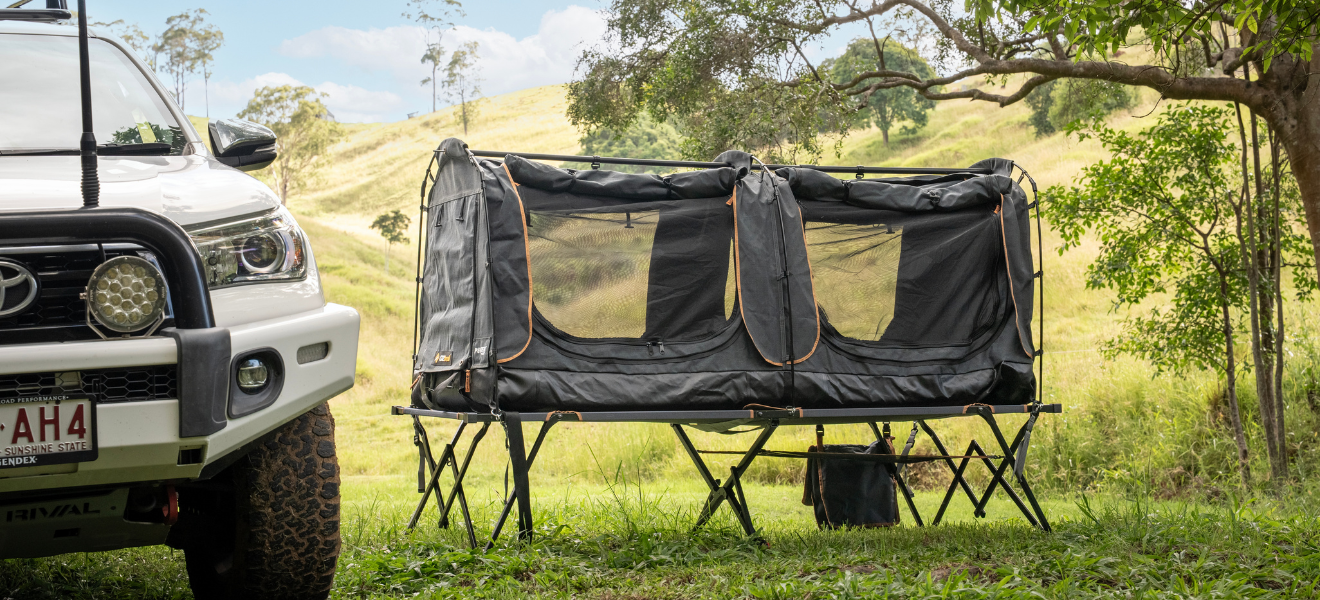 OZtrail Sundowner 900 swag on a Sundowner 900 platform beside a white 4WD, green hills behind.