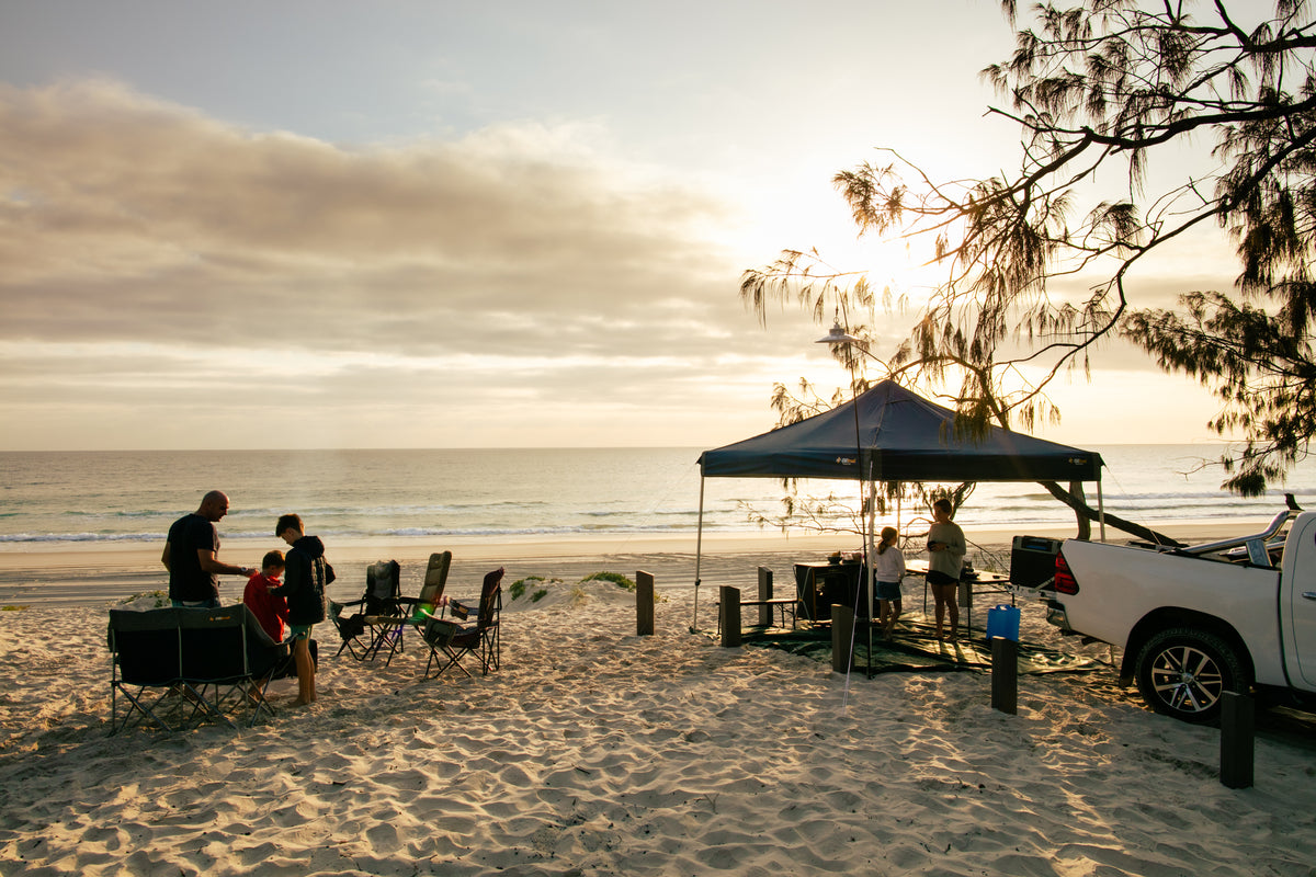 Family camp set up under an OZtrail gazebo on the beach at sunset
