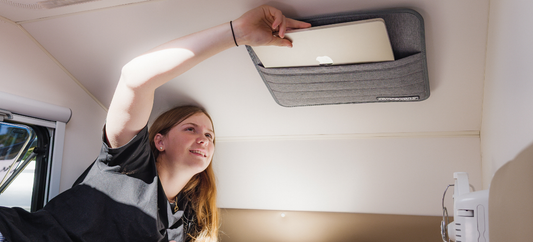 Person placing a laptop into the Caravan Storage Pocket Small mounted on an interior wall.