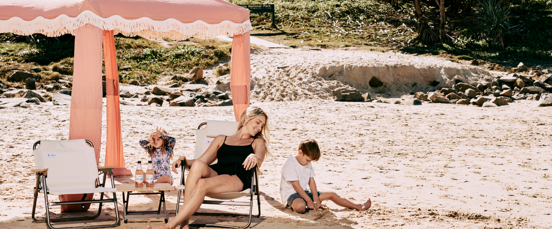 Pink cabana on the beach with a woman lounging in a chair as two children play in the sand