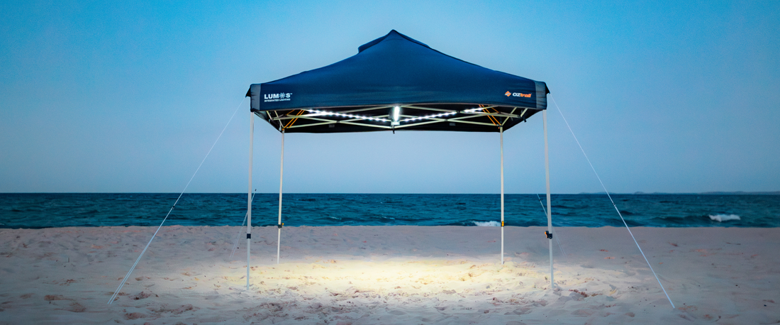 Blockout Lumos 3.0 Navy Gazebo lit up on the beach at dusk, with integrated LED lighting illuminating the sand.