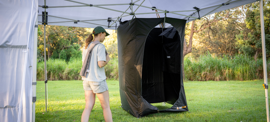 A woman approaches the Deluxe Gazebo BlockOut Ensuite set up beside a canopy in a grassy campsite.