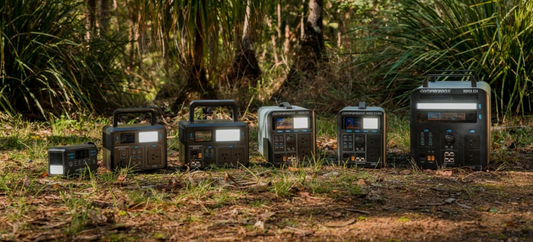 Six Companion Rover portable power stations lined up on the ground in the bush, from the small Rover Go NXT to the large Rover X24, with their LED lights on.