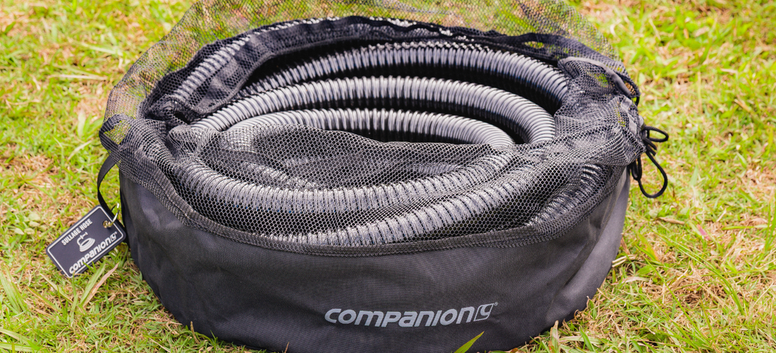Companion sullage hose neatly coiled in a mesh storage bag on grass for easy caravan waste water management.