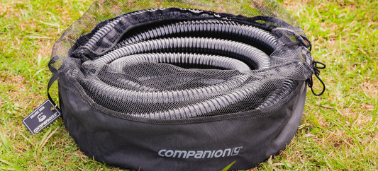 Companion sullage hose neatly coiled in a mesh storage bag on grass for easy caravan waste water management.