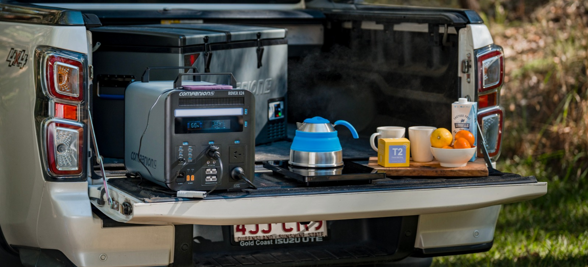 Companion Rover X24 power station on a ute tailgate, running an induction cooktop boiling a kettle, with a portable fridge behind