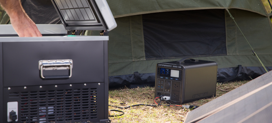 Hand reaching into portable fridge beside tent, powered by Rover 1300 power station