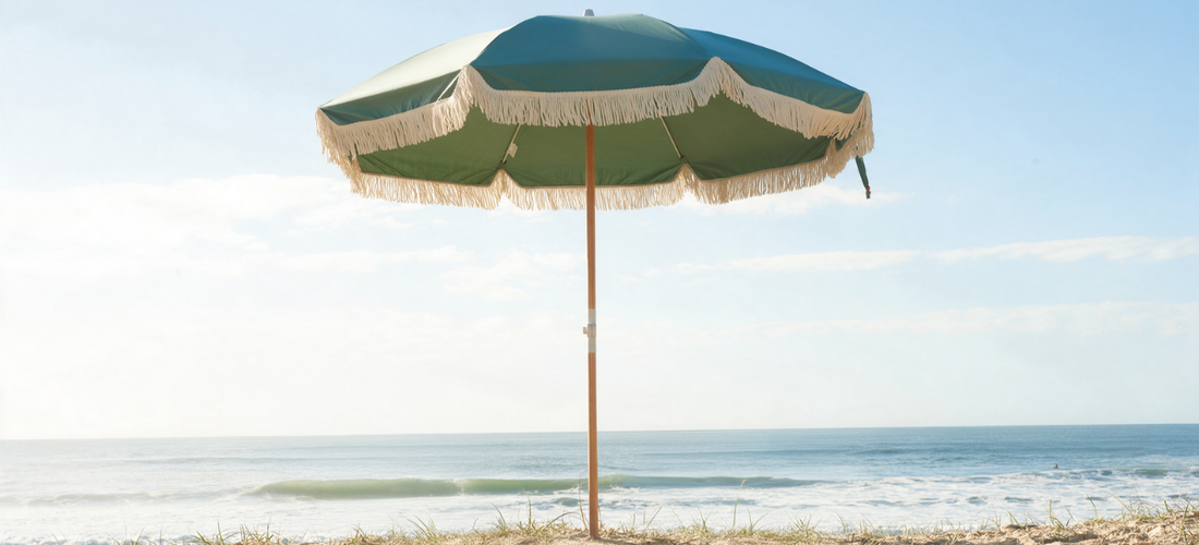 Green beach umbrella in middle with blue skies anchored in sand