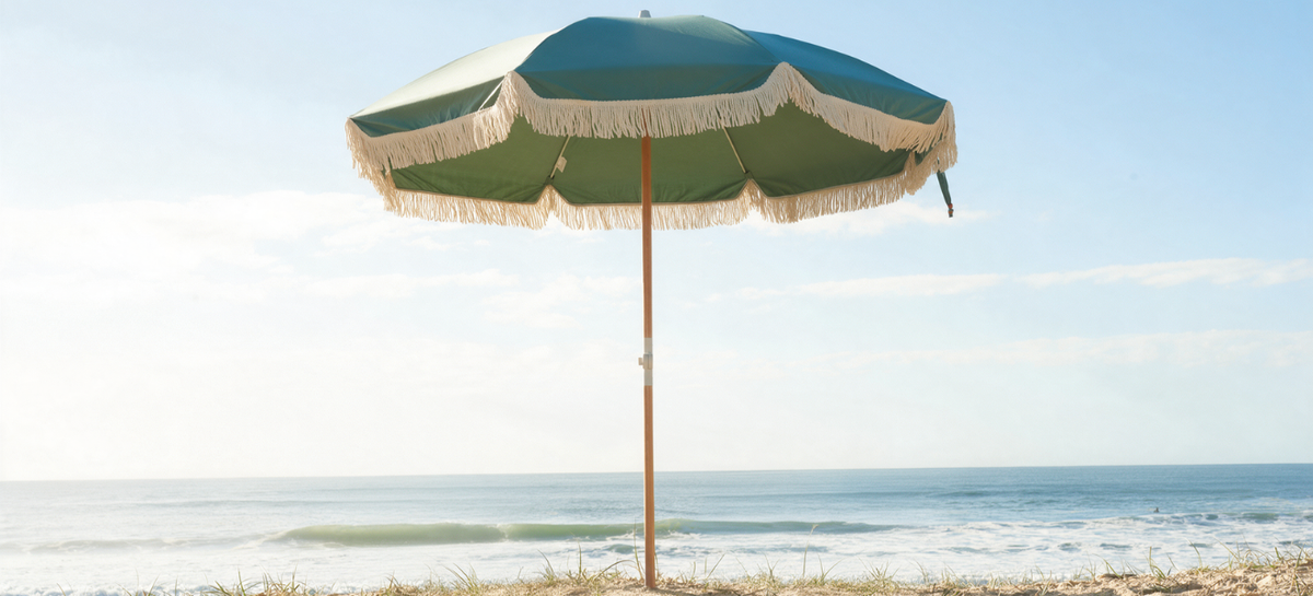 Green beach umbrella in middle with blue skies anchored in sand