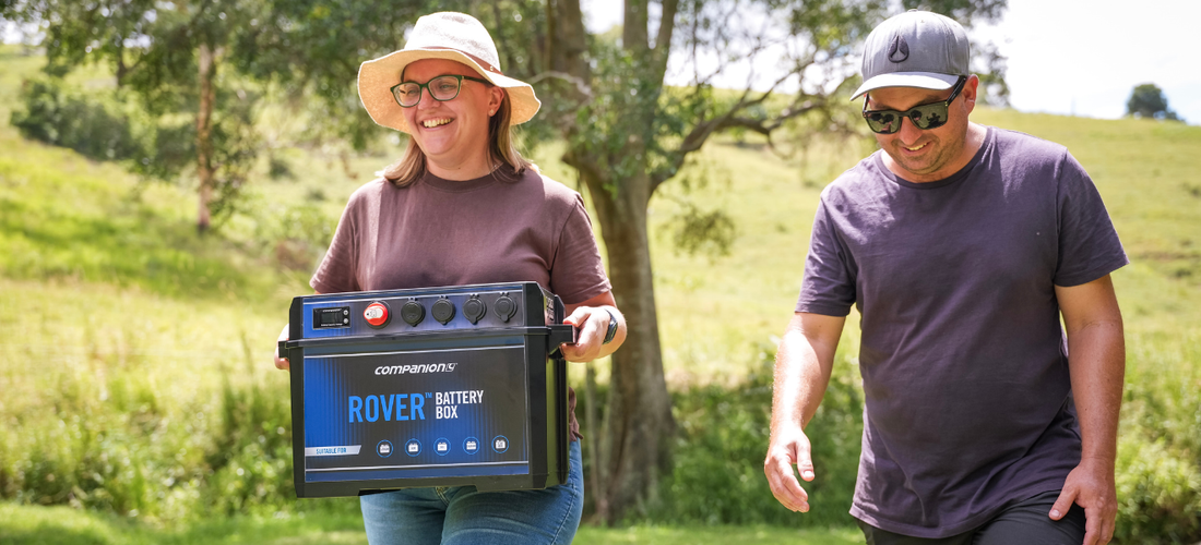 Woman in hat holding Rover battery box smiles as man in sunglasses walks beside her outdoors