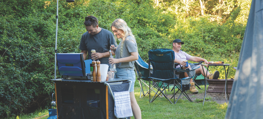 Deluxe Kitchen with Sink set up at a campsite, with campers preparing food while others relax by the fire.